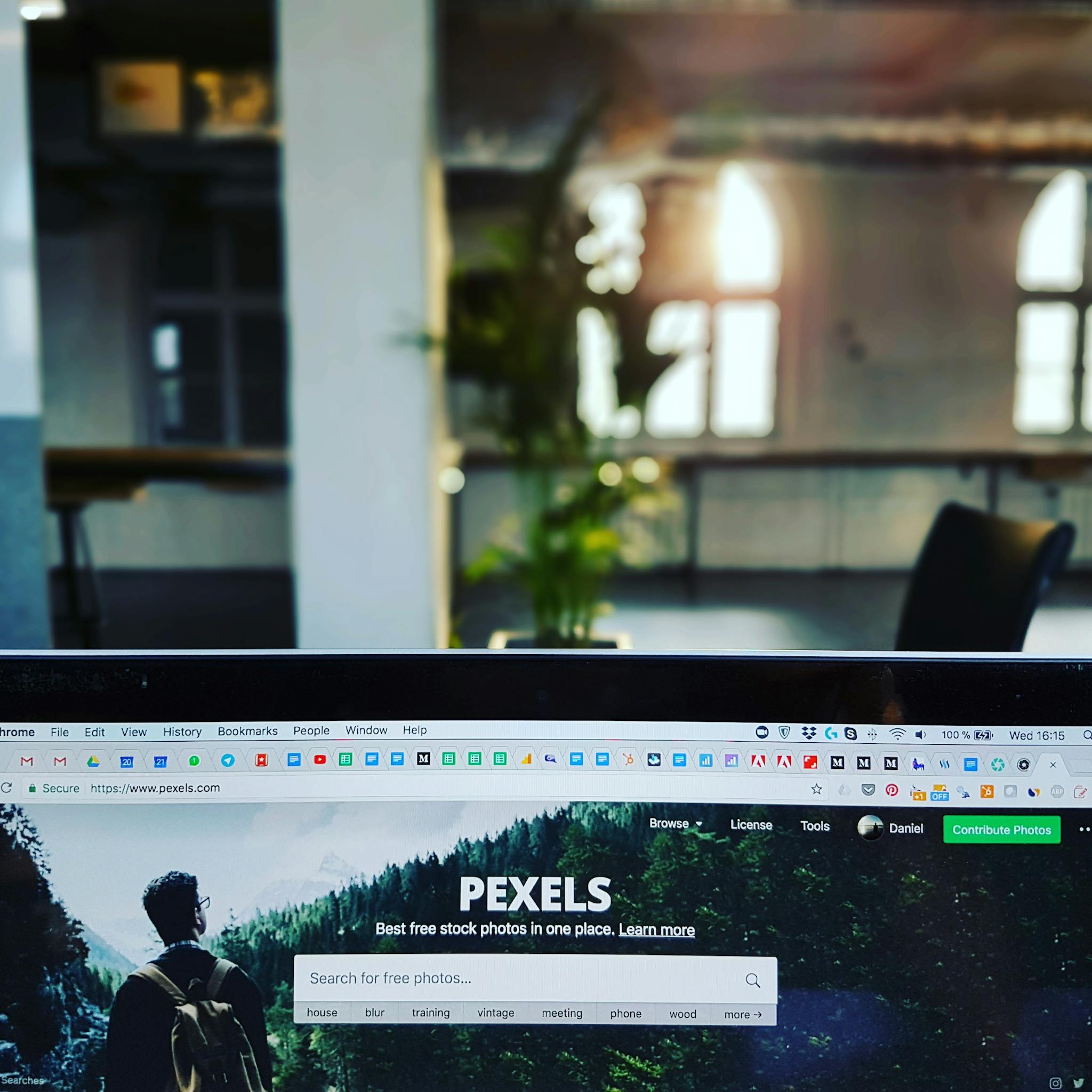 A close-up of a laptop displaying the Pexels website in a sunlit, modern office.